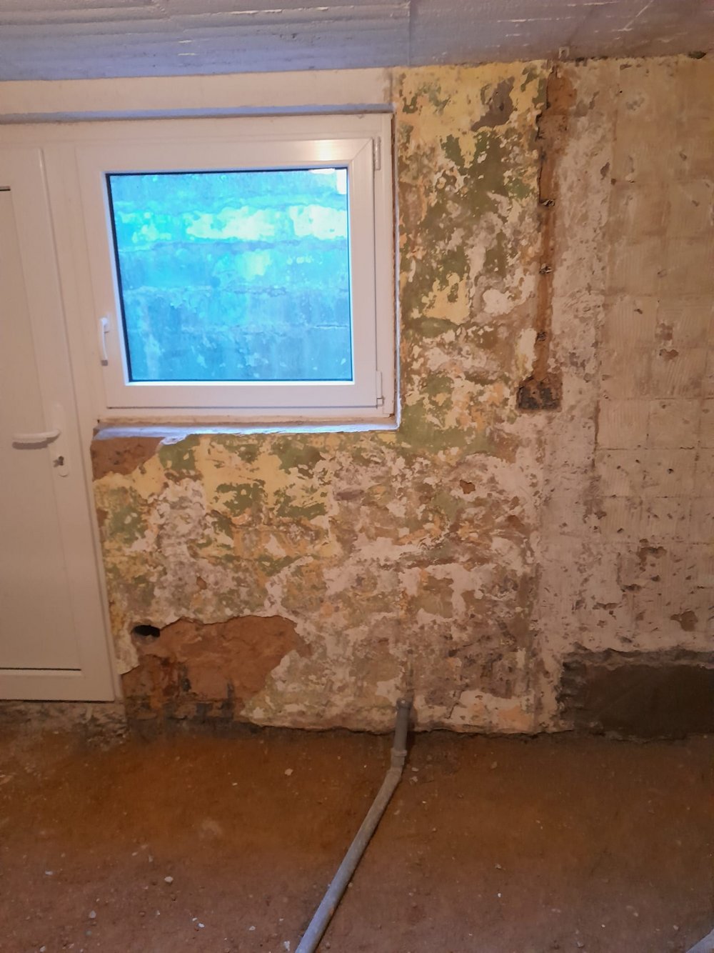 Abgeplatzte Kellerwand mit freiliegender Mauerfläche unter Fenster