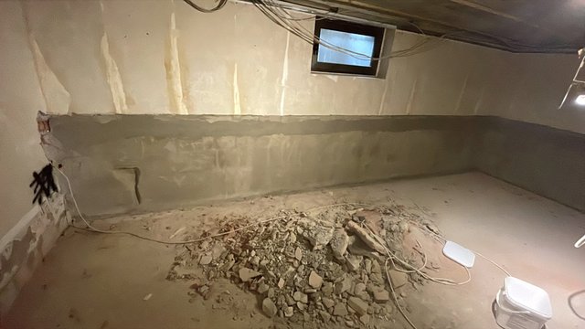 Kellerwand mit grauer Masse beschichtet, Bauschutt liegt auf dem Boden