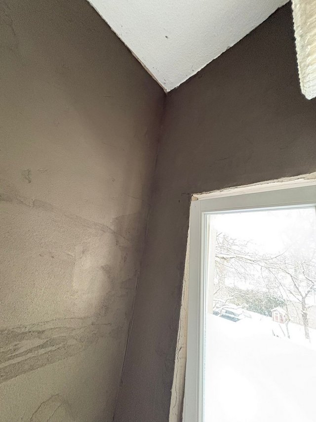 Dunkle Feuchtspur an verputzter Raumecke neben Fenster