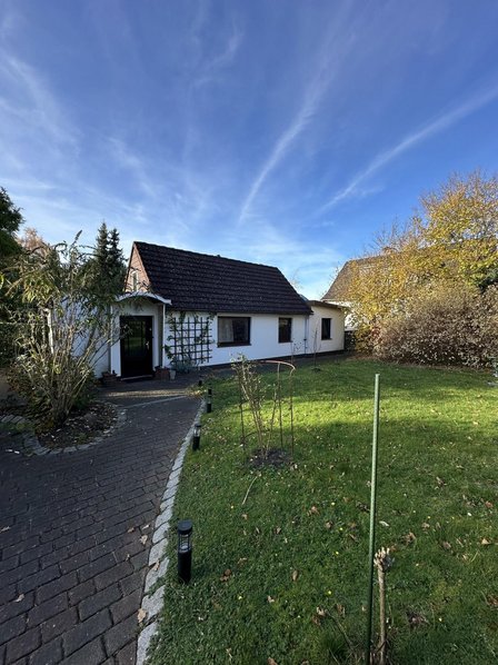 Einfamilienhaus mit Vorgarten, gepflastertem Weg und blauem Himmel