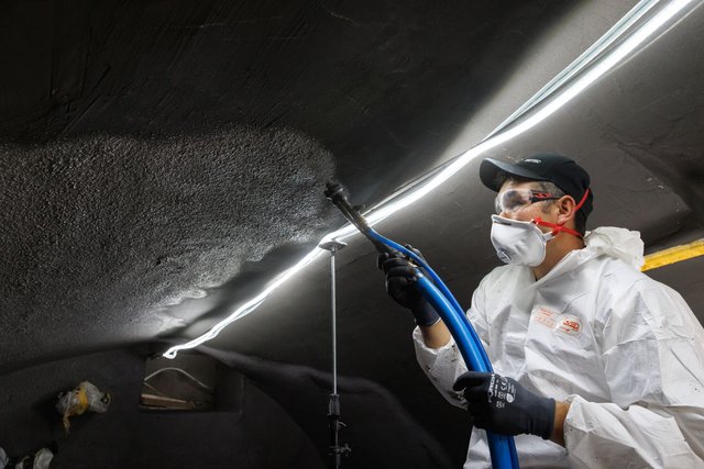 ISOTEC Mitarbeiter sprüht schwarze Masse an eine Decke, Schutzanzug und Atemmaske
