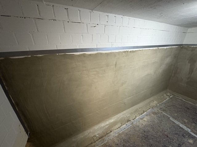 Kellerwand mit hellbeiger Masse beschichtet, darüber weiße Mauersteine und grauer Streifen
