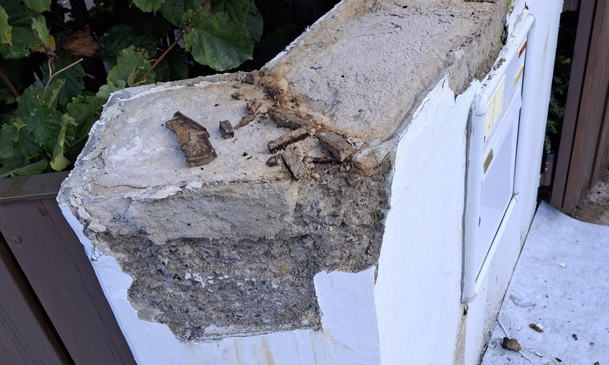 Abgeplatzter Beton an weißem Pfeiler mit Bauschutt, Nahaufnahme