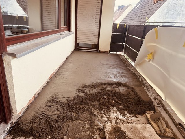 Balkonboden mit frischem grauem Estrich und Werkzeug, teils mit Folie abgedeckt
