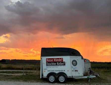 ISOTEC Anhänger steht auf Feldweg vor orangem Sonnenuntergangshimmel