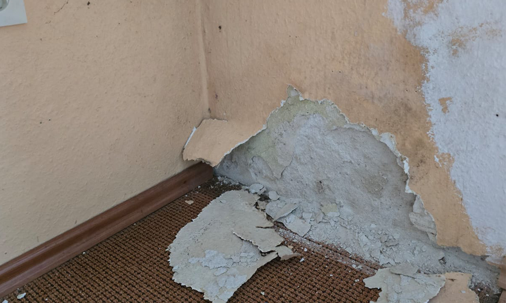 Abblätternde Beschichtung an Zimmerecke mit freiliegender hellgrauer Fläche