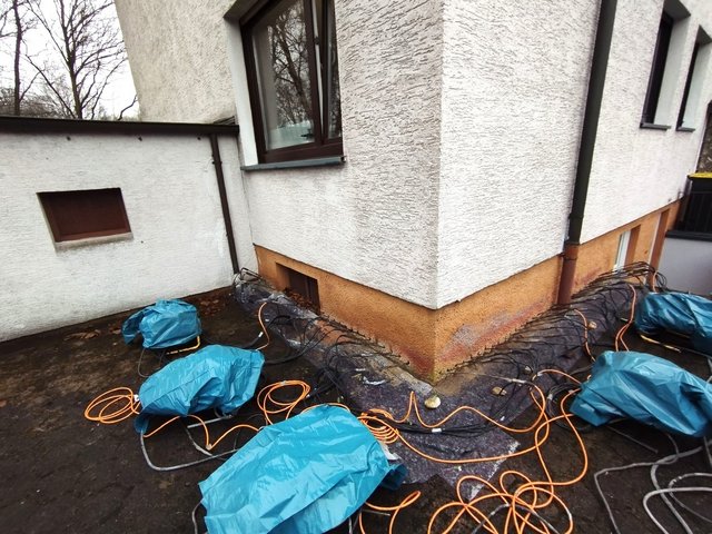 Gebäudeecke mit Kabeln und abgedeckten Geräten am Sockel