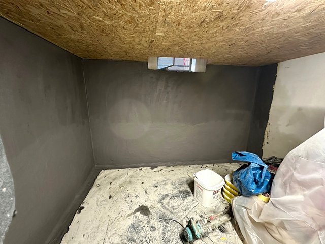 Kellerraum mit grauer Wandbeschichtung, OSB-Decke und kleinem Fenster, Werkzeuge am Boden.