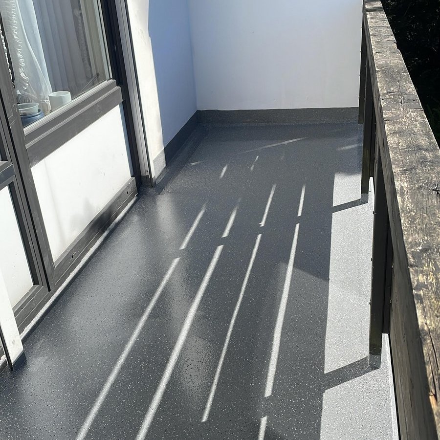 Schmaler Balkon mit grauem Bodenbelag und Holzgeländer in Sonnenlicht