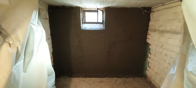 Kellerraum mit frisch verputzter dunkelgrauer Wand und kleinem Fenster