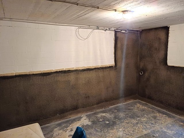 Kellerwand mit schwarzer Masse im unteren Bereich und weißem Mauerwerk darüber