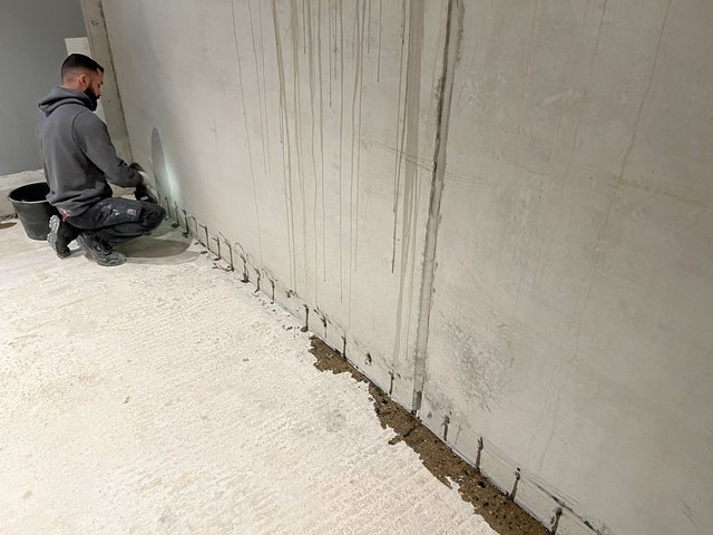 Arbeiter bohrt Löcher am unteren Rand einer Kellerwand.