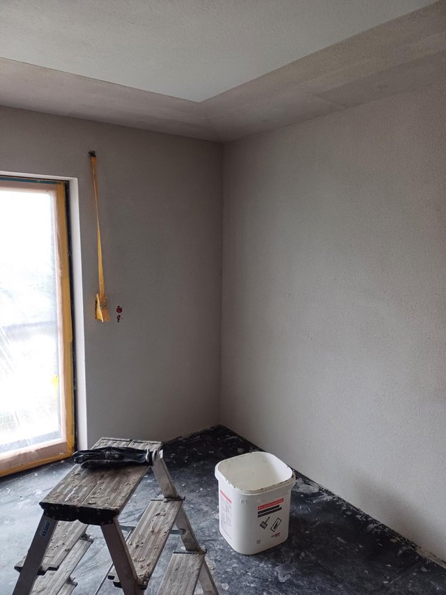 Raum mit grauen Wandflächen, Leiter und Eimer auf dunklem Boden