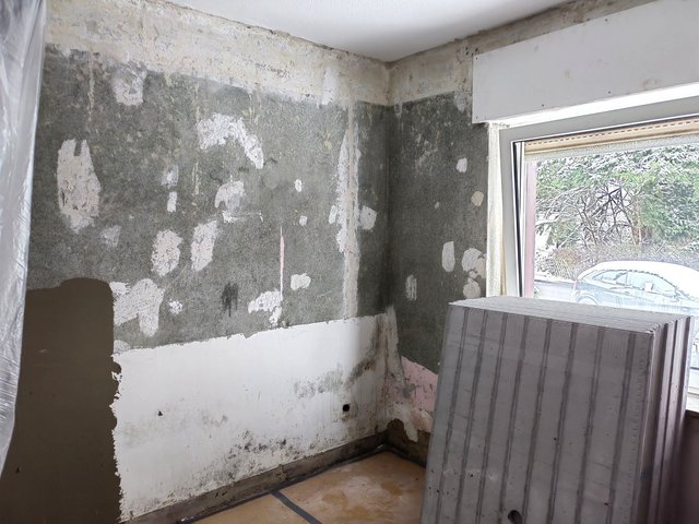 Freigelegte Zimmerwand mit dunklen Feuchtespuren und heller Platte am Fenster