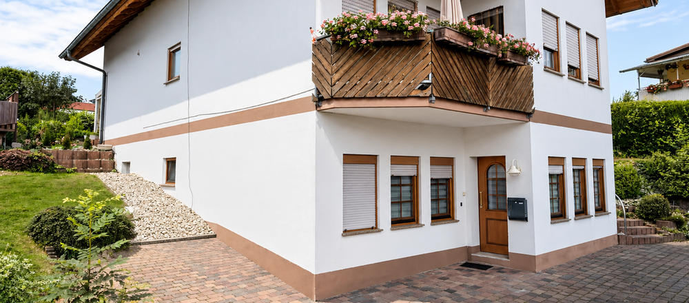 Weißes Wohnhaus mit Holz-Balkonen, Blumenkästen und gepflasterter Einfahrt