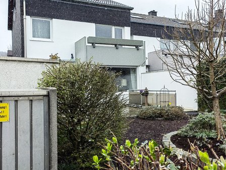 Verschneiter Garten vor mehrstöckigem Wohnhaus mit Sträuchern und Terrasse