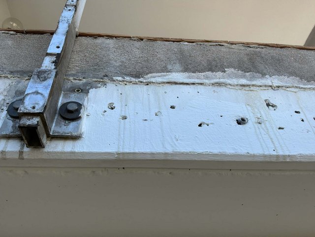 Stahlträger mit Schrauben auf weiß beschichteter Betonfläche, Bohrlöcher sichtbar