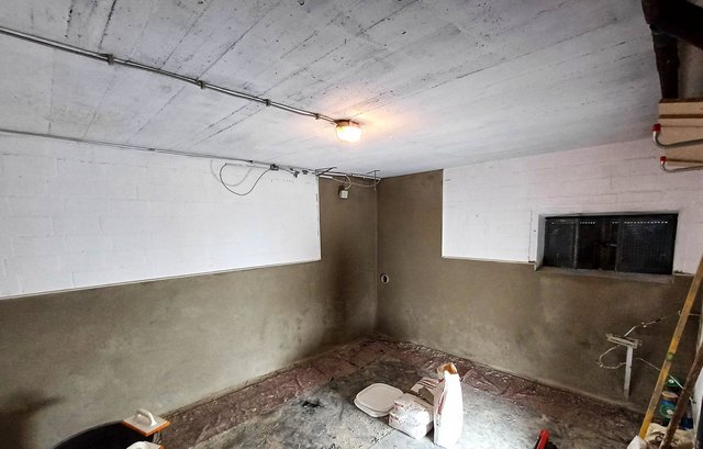 Kellerraum mit grauer Masse im unteren Wandbereich und kleinem Fenster