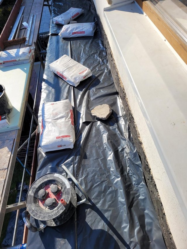 Abgedeckter Balkonboden mit Säcken, Werkzeug und losem Betonstück neben Fensterbank