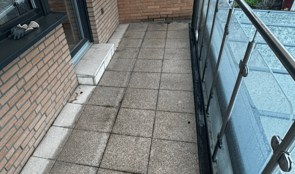 Balkon mit Steinplatten, Ziegelwand, Glasschiebefenster und Glasgeländer, Nahansicht