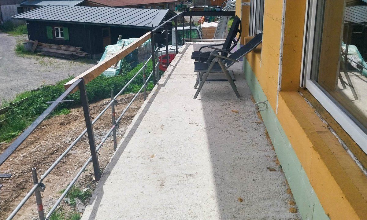 Balkon mit Betonboden und Stahlgeländer an gelber Fassade mit Dämmung