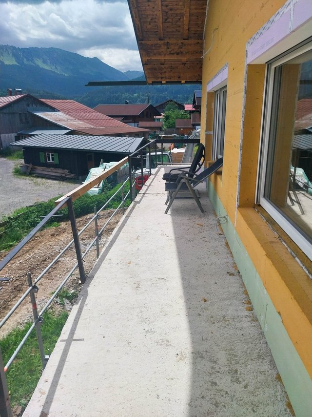 Balkon mit Betonboden und Stahlgeländer an gelber Fassade mit Dämmung