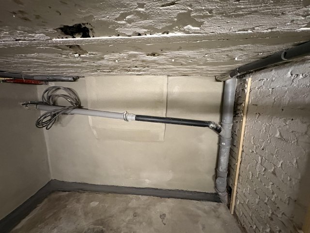 Kellerraum mit freigelegten Rohren, verputzter Wand und beschädigter Decke