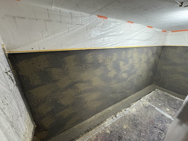 Abgeklebte Folie über schwarzer Masse auf Kellerwand, Sanierungsbereich