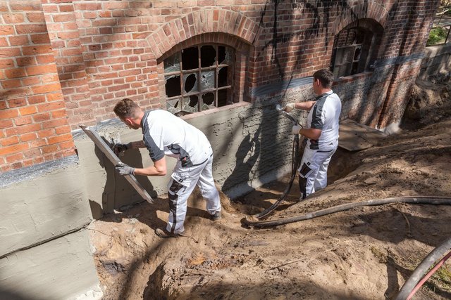 Handwerker beim Ausführen einer Außenabdichtung am Keller, um Feuchtigkeitsschäden effektiv zu verhindern