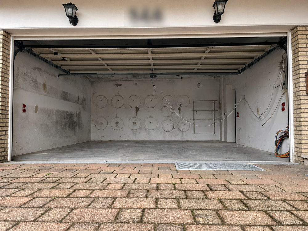 Leere Garage mit offenen Tor, schmutzigen Wänden, freihängenden Kabeln und Betonboden