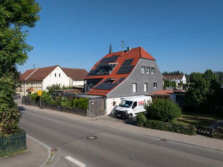 Wohnhaus mit Solarpaneelen auf rotem Ziegeldach, ISOTEC Transporter am Straßenrand