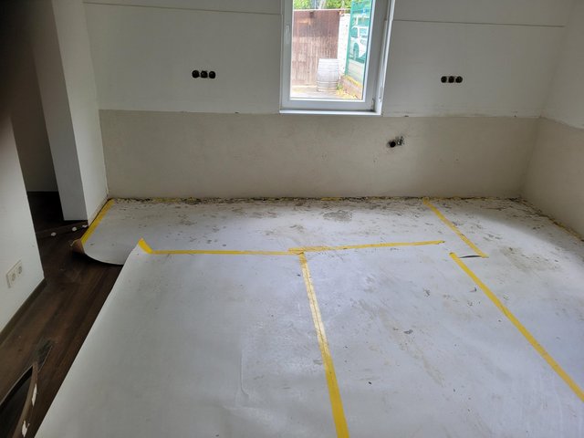 Abgedeckter Boden mit Folie und Klebeband, Fenster und freigelegte Wandanschlüsse.