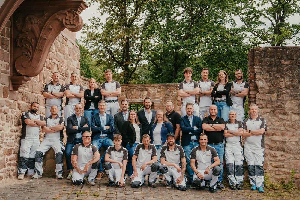 ISOTEC Teamfoto vor Steinmauer, Mitarbeiter in Arbeitskleidung und Business-Outfits im Freien