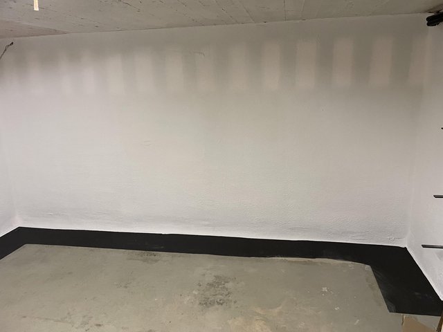 Weiße Kellerwand mit schwarzem Randstreifen am Boden