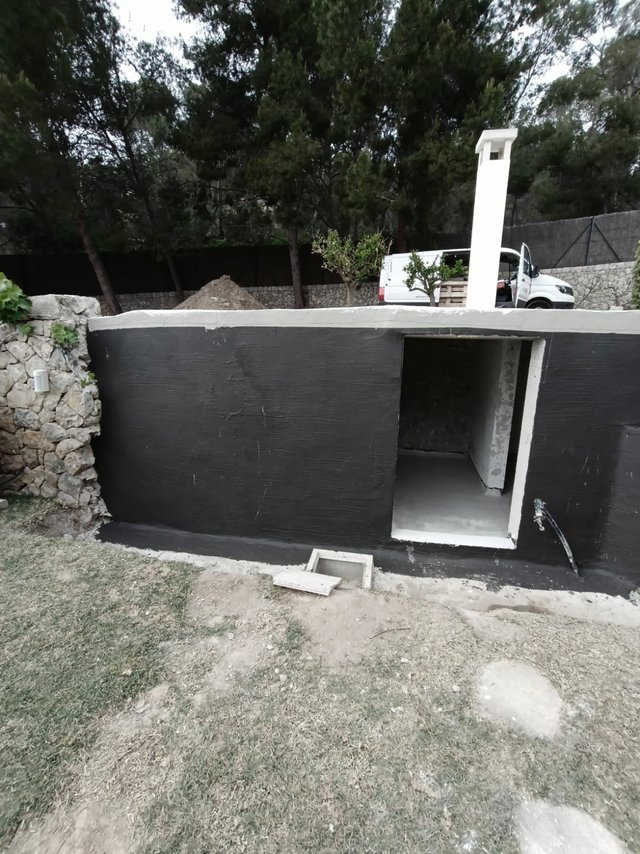Schwarze Beschichtung auf Betonwand mit offener Nische und Ablaufhahn im Garten