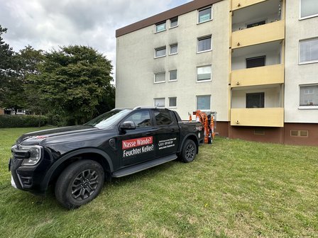ISOTEC Transporter mit Anhänger steht vor Mehrfamilienhaus auf Rasenfläche.