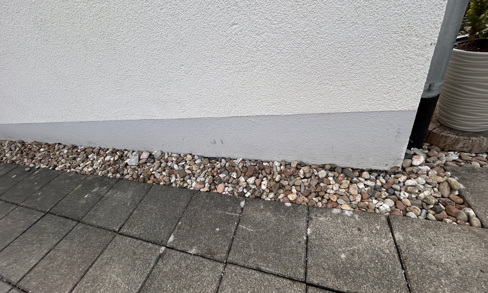 Weiße Fassade mit grauem Sockel, Kiesstreifen und Pflastersteinen