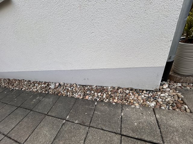 Weiße Fassade mit grauem Sockel, Kiesstreifen und Pflastersteinen