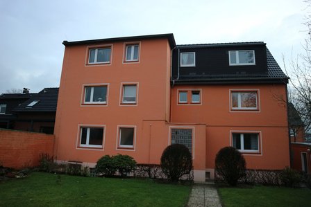 Orangefarbenes Wohnhaus mit weißen Fenstern und Vorgarten, Frontansicht.