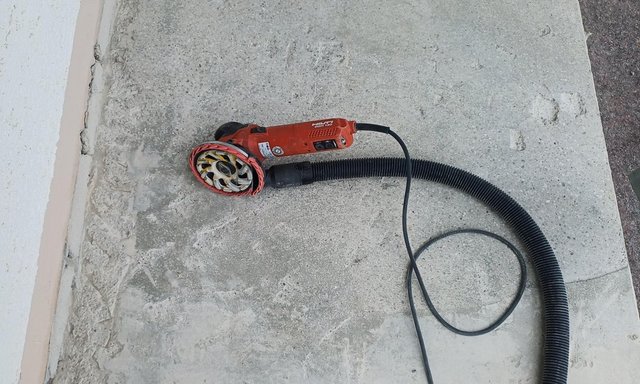 Bodenschleifer mit Absaugschlauch auf grauer Betonfläche neben Rollladen