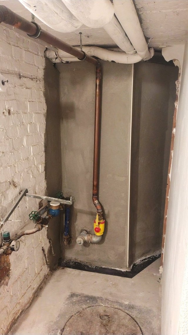 Kellerraum mit Rohren und Armaturen vor grauer Masse an Wand und Sockel