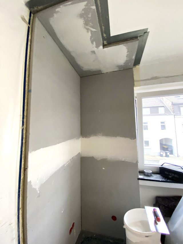 Renovierte Raumecke mit grauen Wandflächen, Decke mit Spachtelstellen und Fensterbank