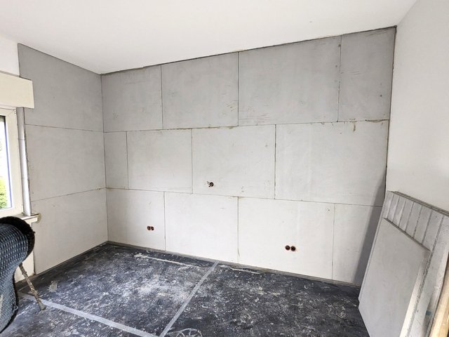Zimmer mit hellen Wandplatten und freiliegenden Steckdosenöffnungen, Boden abgedeckt