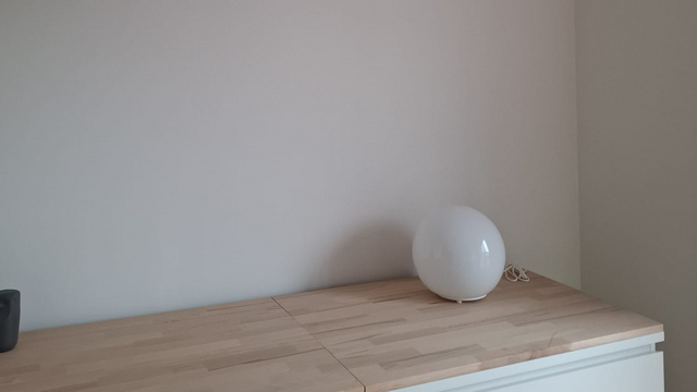 Weiße Kugellampe auf hellem Holzschrank vor glatter Wand