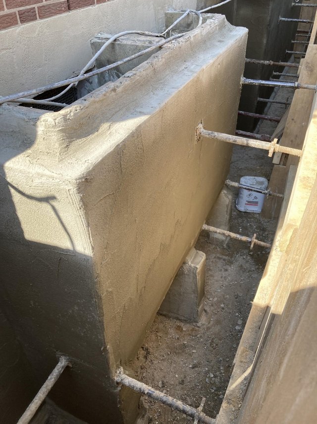Frisch beschichtete Betonkante in Baugrube mit Gerueststangen und Kabeln.