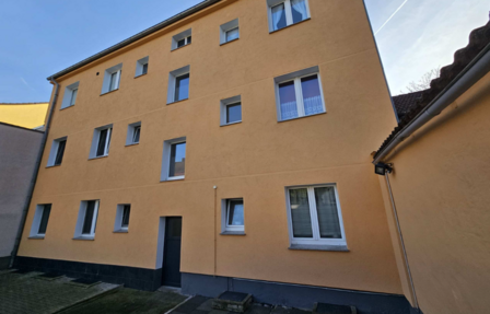 Mehrstöckiges Wohngebäude mit ockerfarbener Fassade, Innenhofansicht mit Fenstern und Eingangstür.