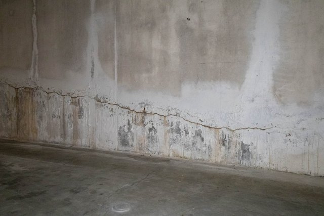 Betonwand mit Riss und dunklen Feuchteflecken am unteren Bereich
