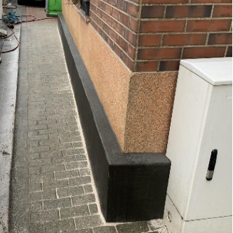 Schwarze Masse am Sockel einer Ziegelhauswand, Gehwegansicht