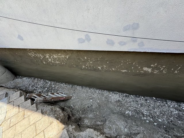 Freigelegte Gebäudewand mit frisch aufgetragener grauer Masse über Erdreich.