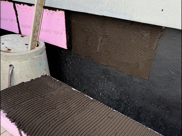 Gerillte braune Masse auf rosa Dämmplatten am Gebäudesockel